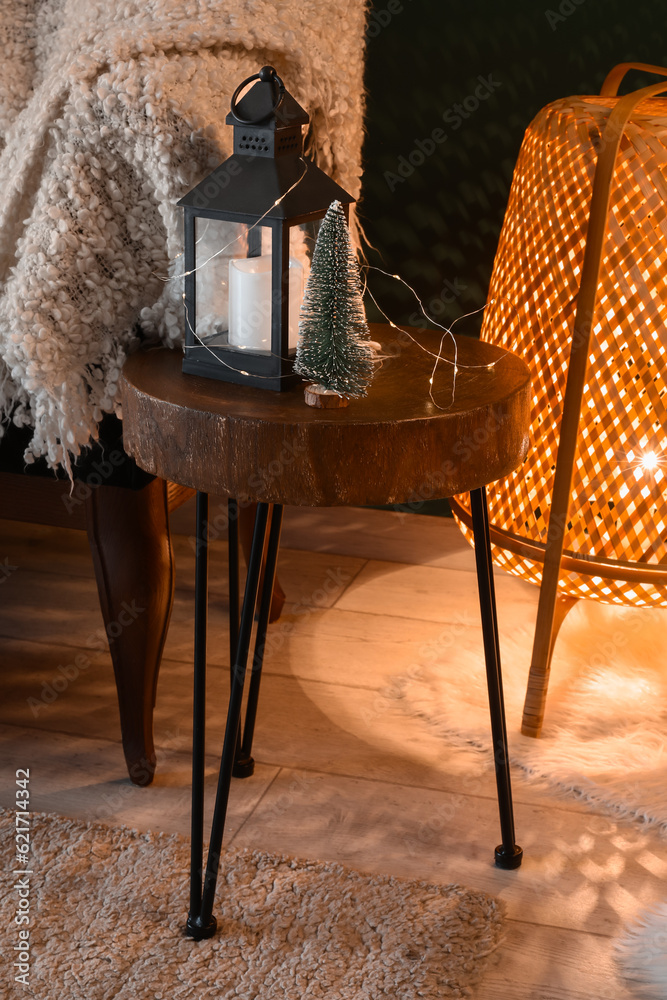 Stool with lantern, small Christmas tree and glowing lights in living room, closeup