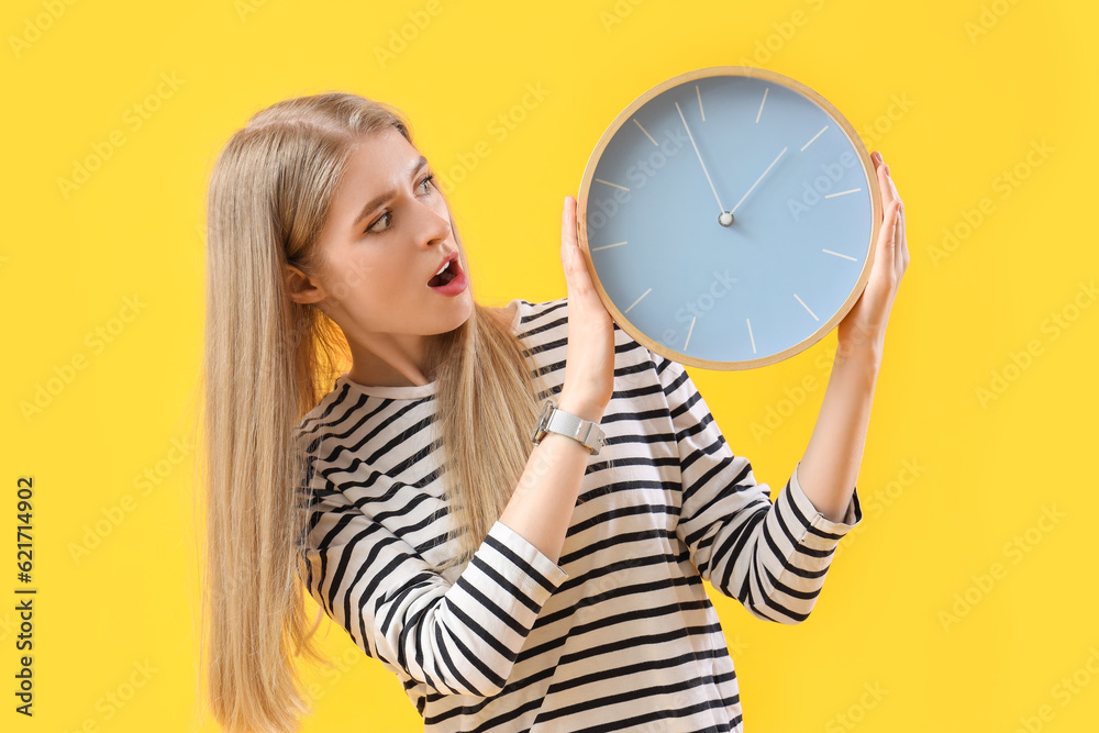 Stressed young woman with clock on yellow background. Deadline concept