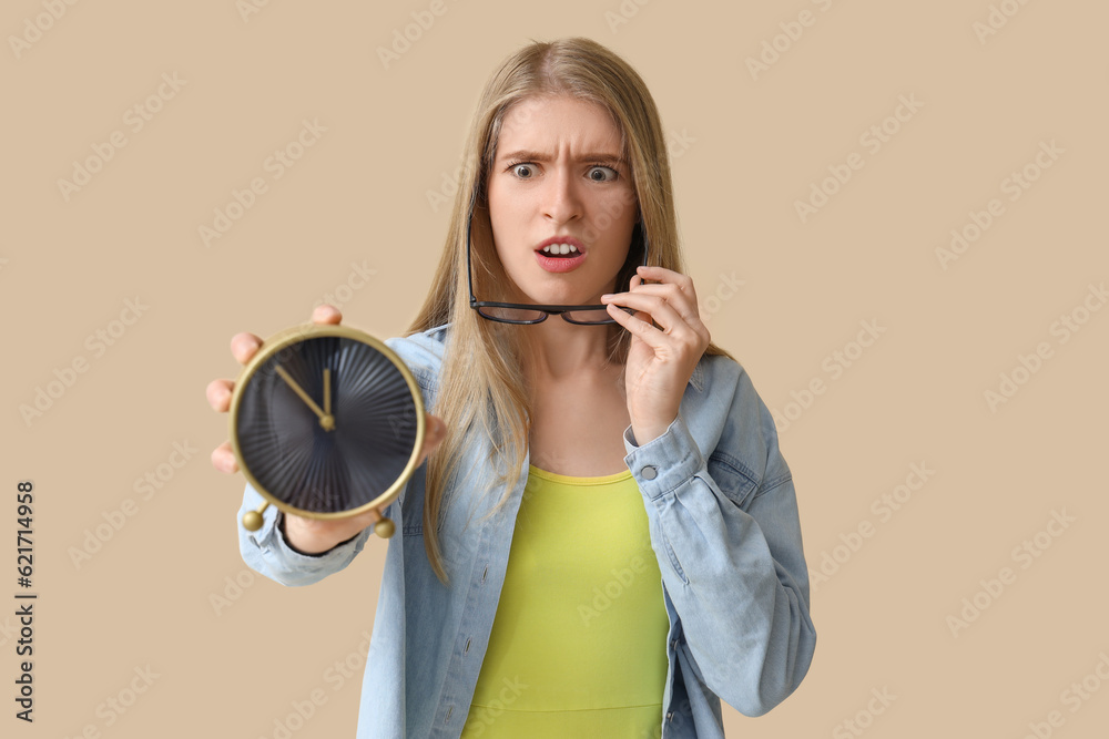 Stressed young woman with alarm clock on beige background. Deadline concept