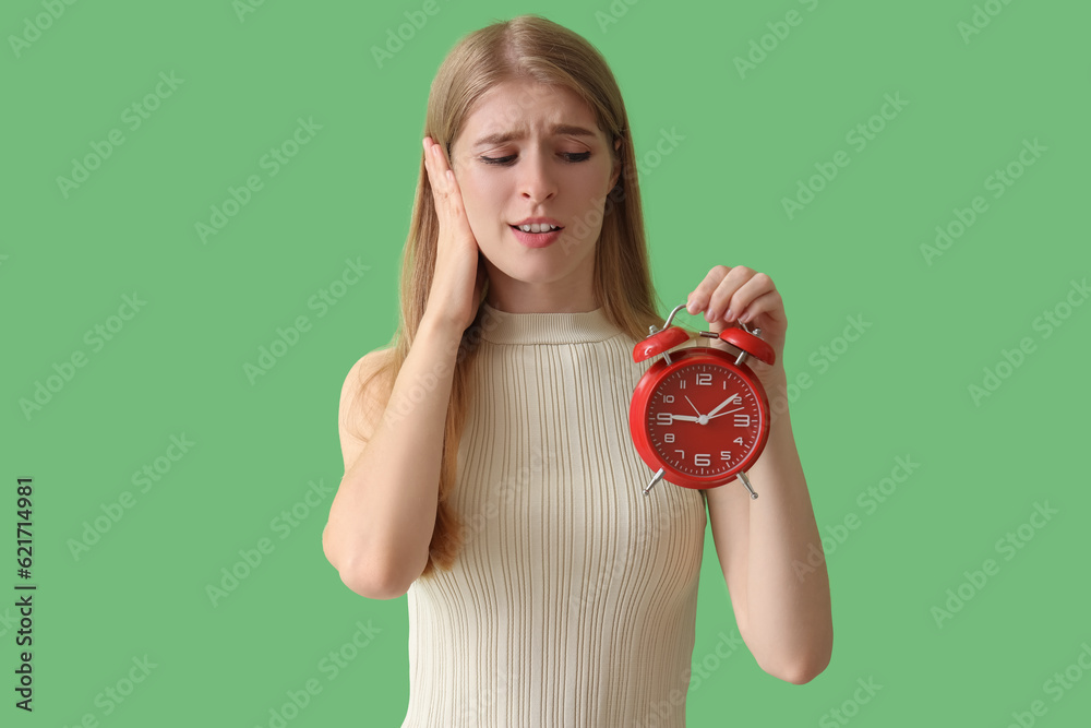 Stressed young woman with alarm clock on green background. Deadline concept