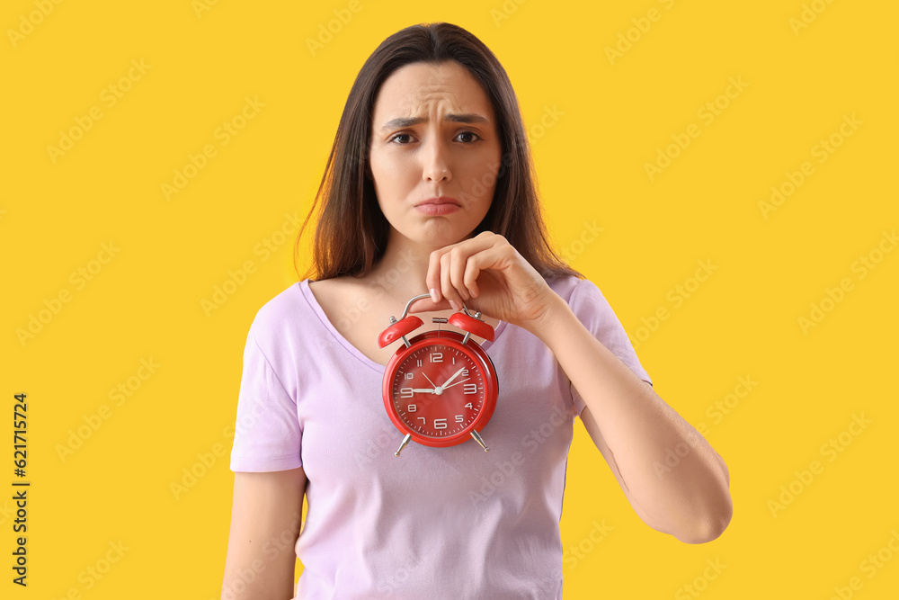 Sad young woman with clock on yellow background. Deadline concept