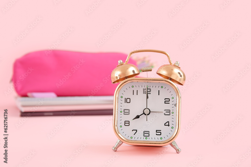 Alarm clock with notebooks and pencil case on pink background