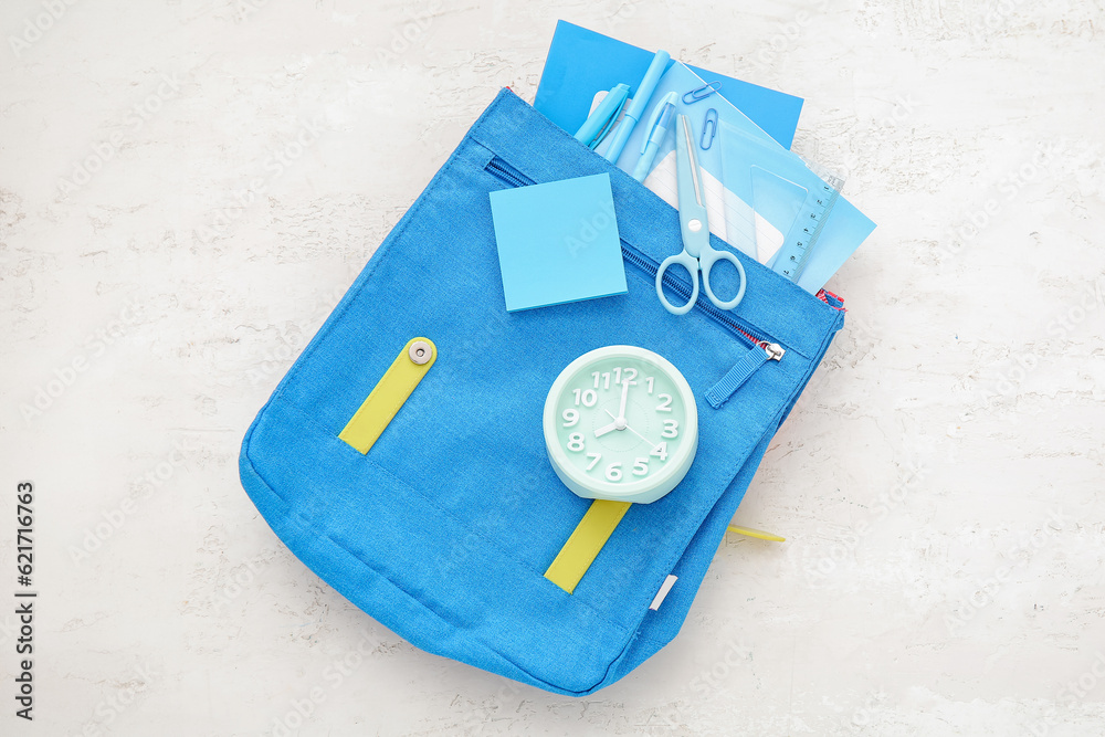 Backpack with alarm clock and different stationery on white background