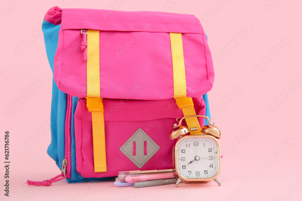 Backpack with alarm clock and stationery on pink background