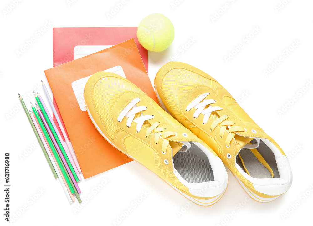 Sneakers with notebooks, colorful pencils and tennis ball isolated on white background