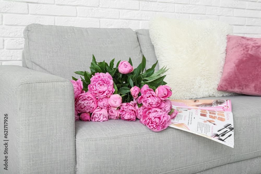 Bouquet of pink peonies with magazine and pillows on couch near white brick wall