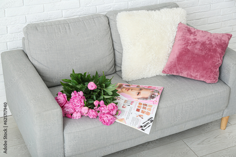 Bouquet of pink peonies with magazine and pillows on couch near white brick wall