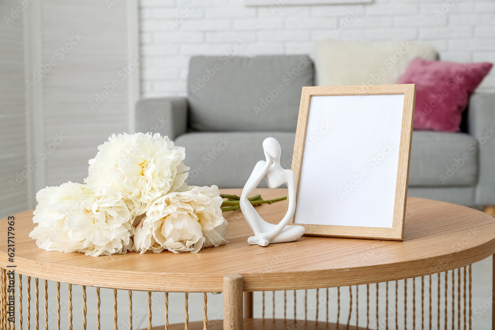 Bouquet of white peonies with photo frame and figurine on coffee table in living room