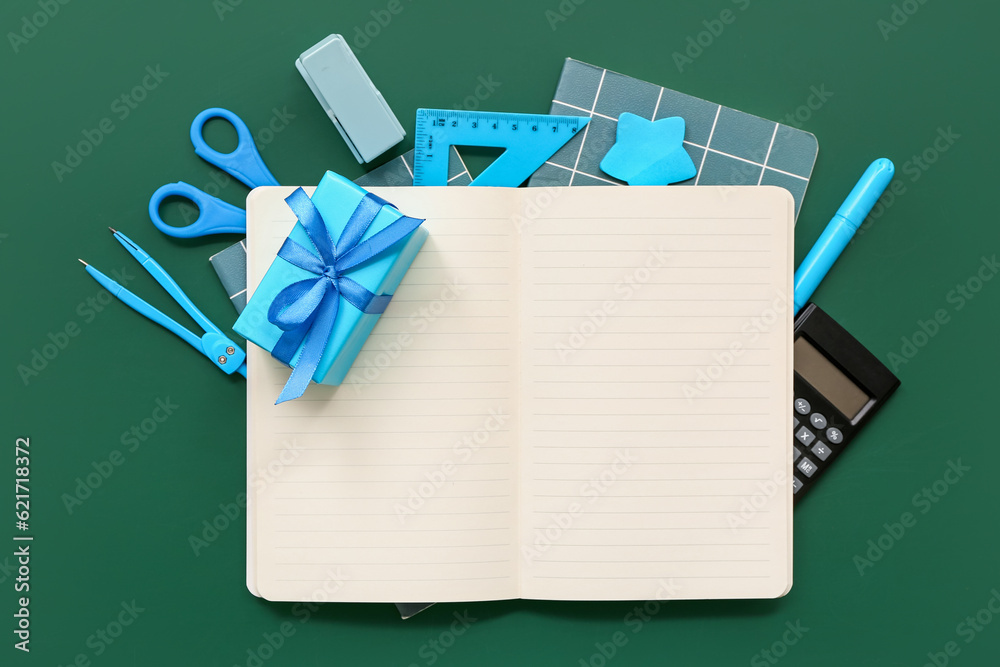 Notebooks with gift box, calculator and different stationery on green chalkboard