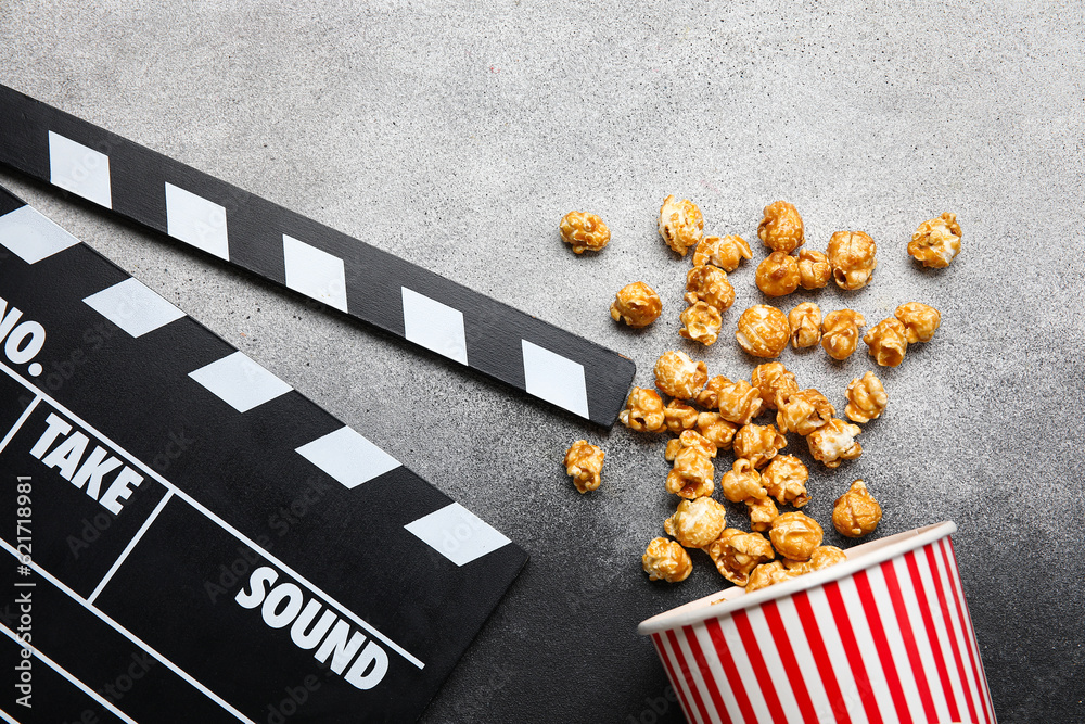 Bucket with tasty popcorn and clapperboard on grey background