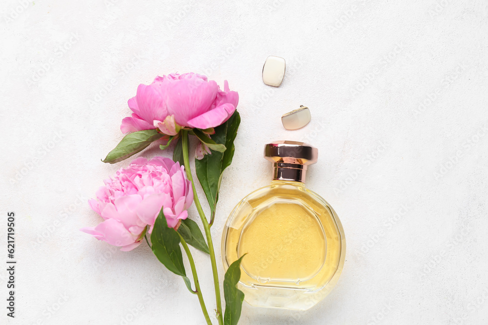 Bottle of perfume, earrings and beautiful peony flowers on light background