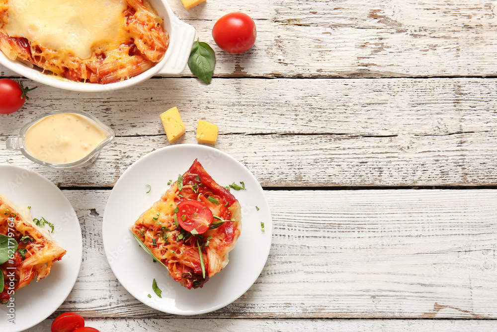 Plates and baking dish of pasta with tomato sauce on white wooden background