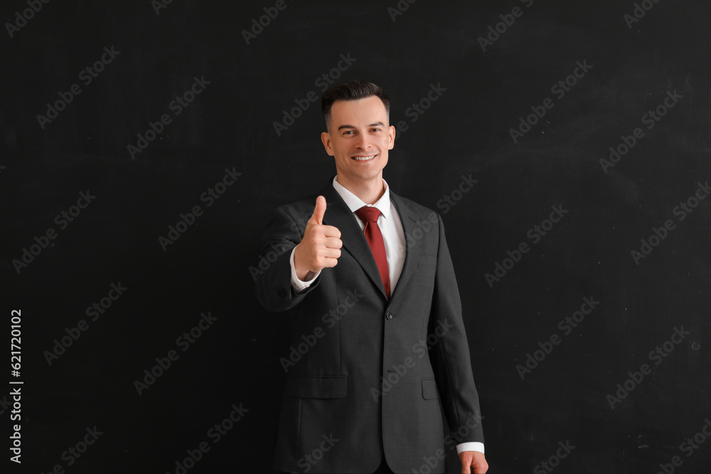 Male teacher showing thumb-up near blackboard in classroom