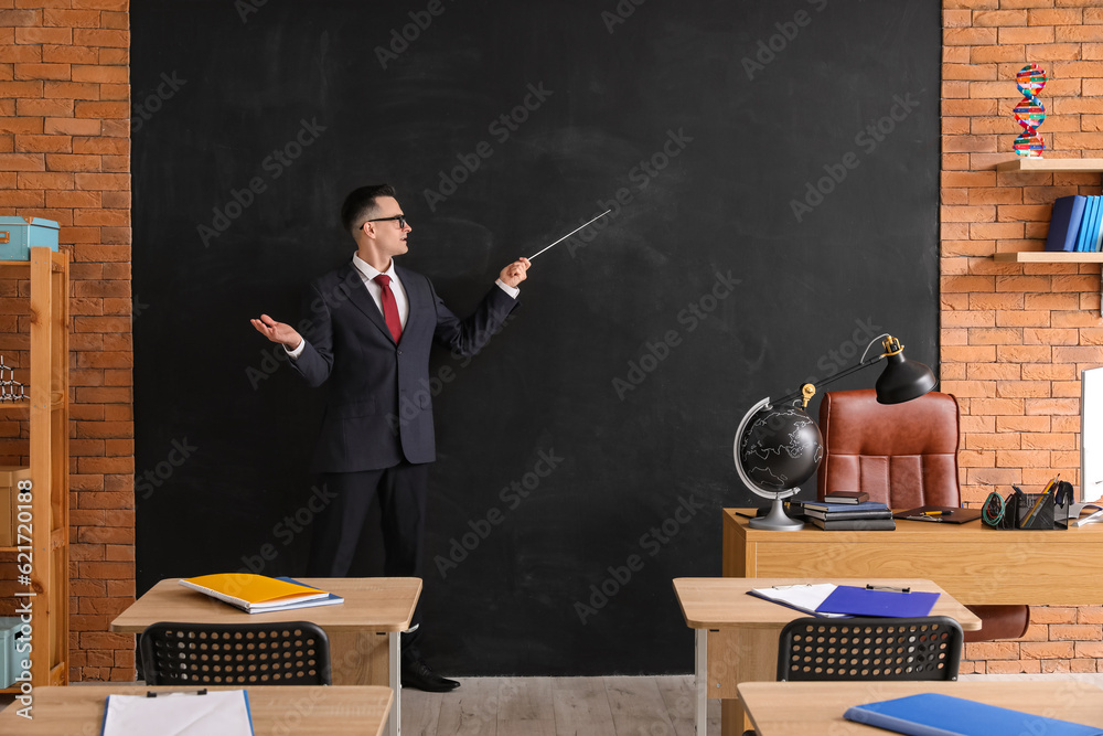 Male teacher with pointer near blackboard in classroom