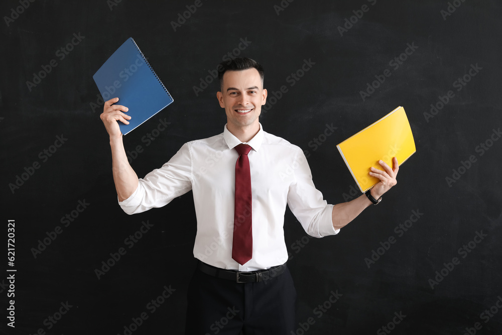 Male teacher with notebooks near blackboard in classroom