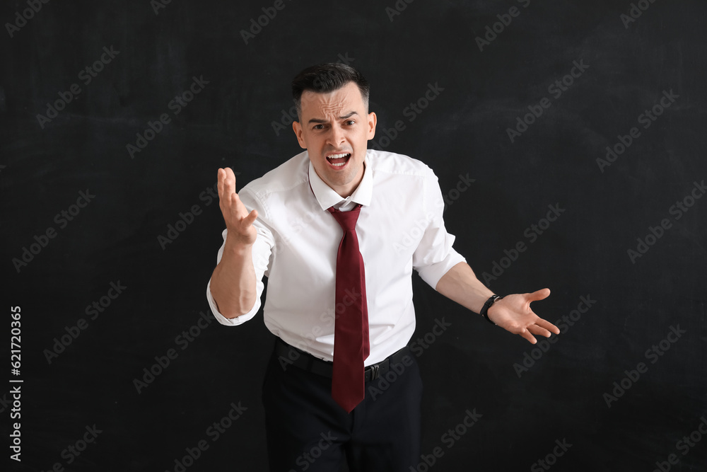 Angry male teacher near blackboard in classroom