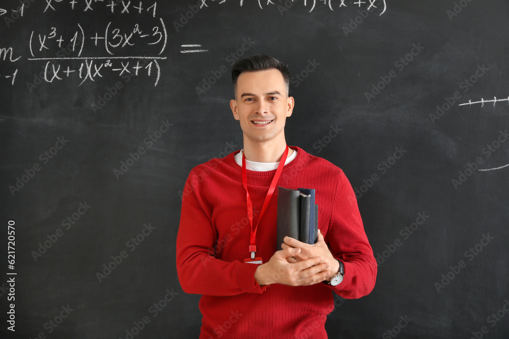 Male Math teacher with books near blackboard in classroom