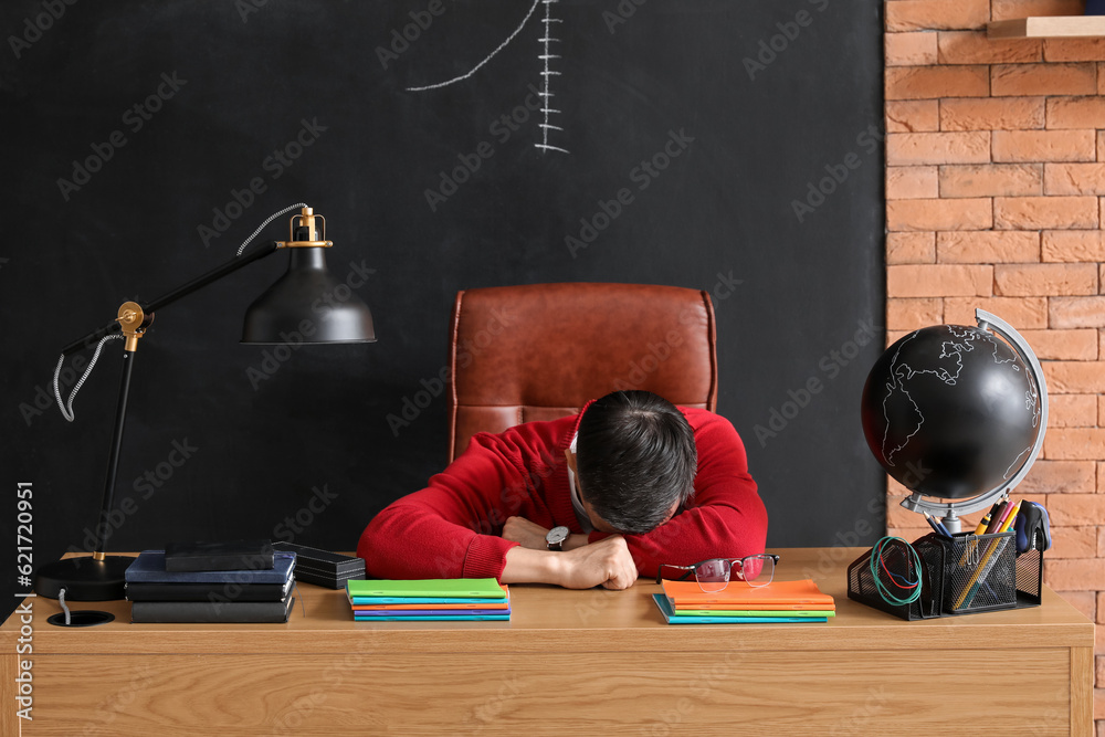 Male teacher sleeping at table in classroom