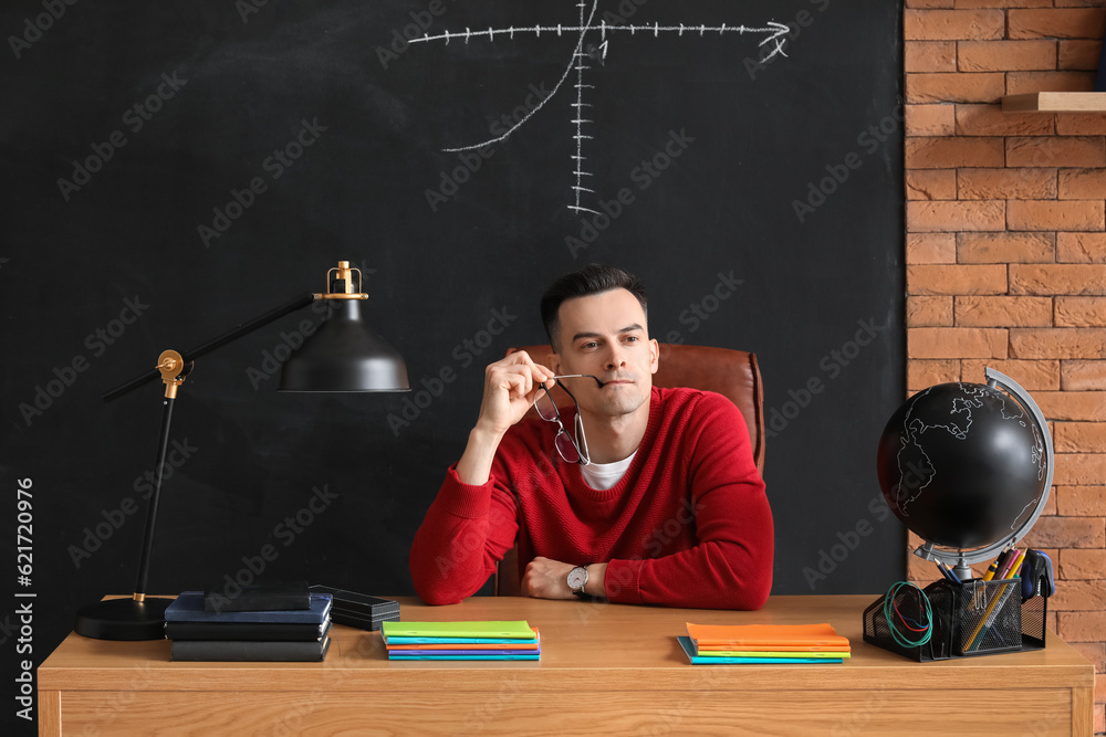 Thoughtful male teacher sitting at table in classroom