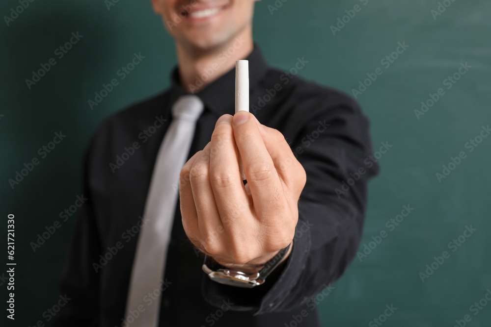 Male teacher with chalk piece near chalkboard, closeup