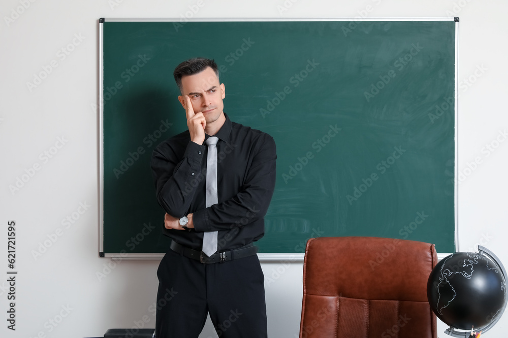 Thoughtful male teacher near chalkboard in classroom