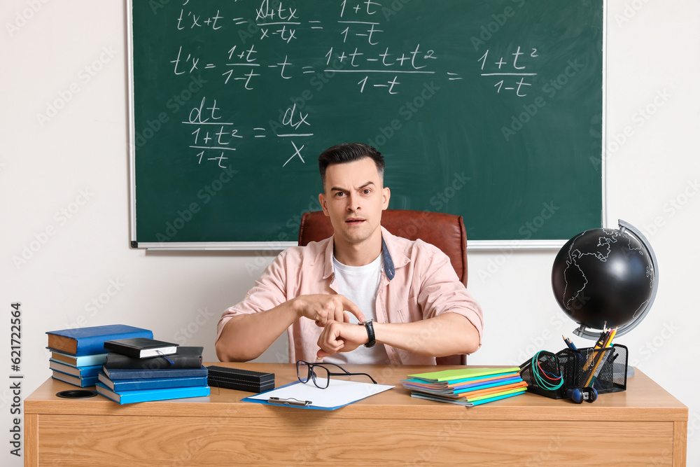 Male teacher looking at wristwatch in classroom