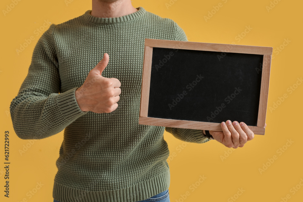 Male teacher with chalkboard showing thumb-up on yellow background, closeup