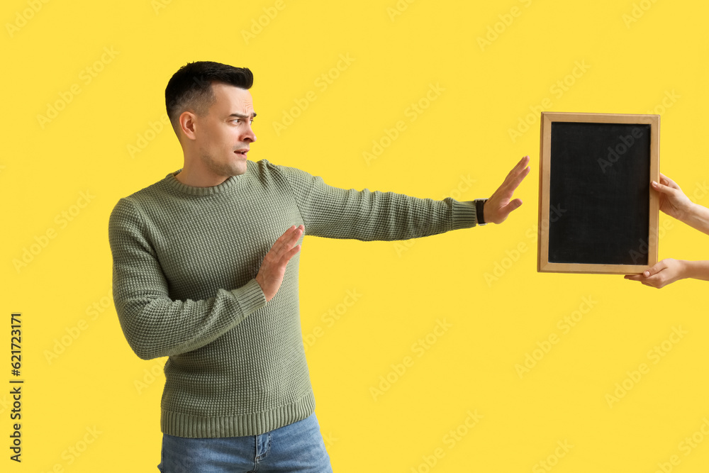 Male teacher rejecting chalkboard on yellow background