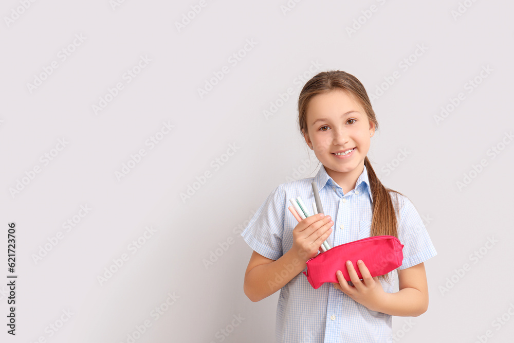 Little girl with pens and pencil case on light background