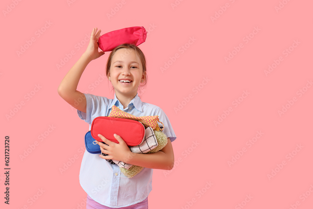 Little girl with pencil cases on pink background