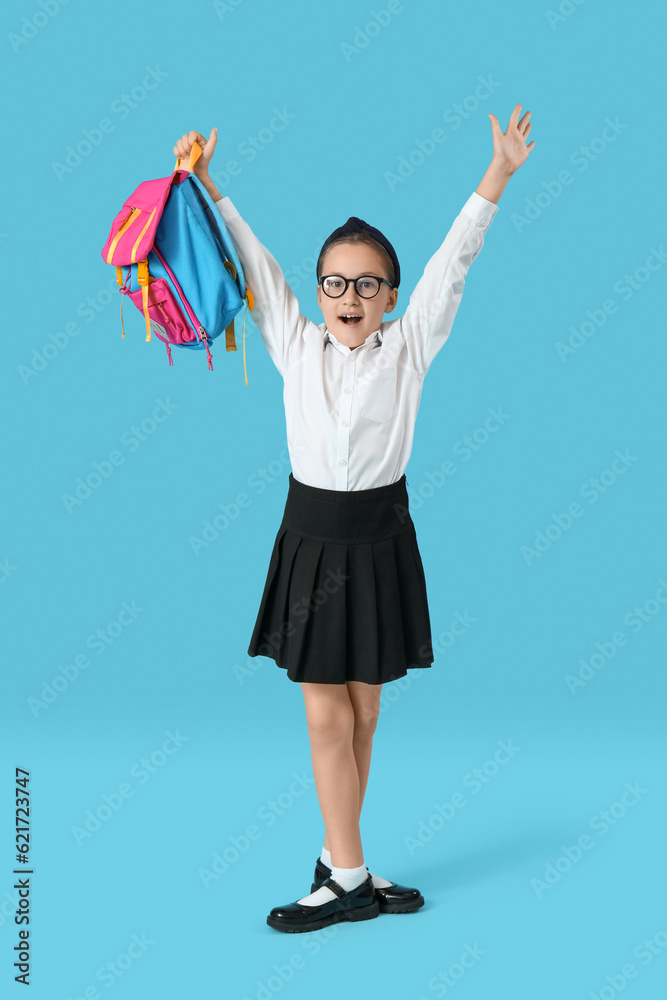 Little schoolgirl with backpack on blue background