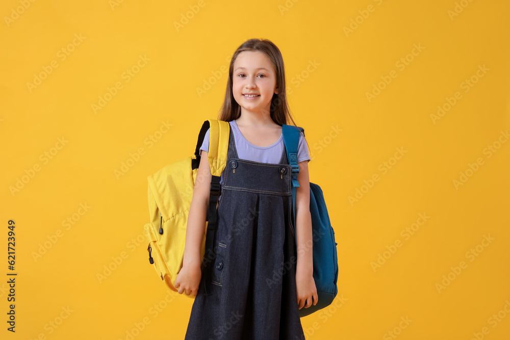 Little girl with backpacks on yellow background