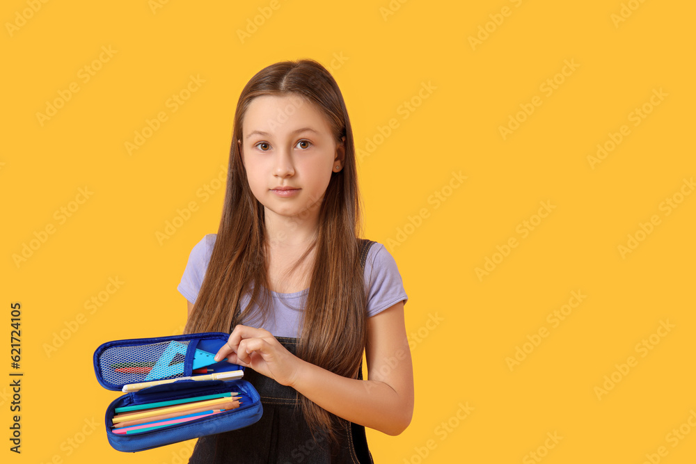 Little girl with pencil case on yellow background