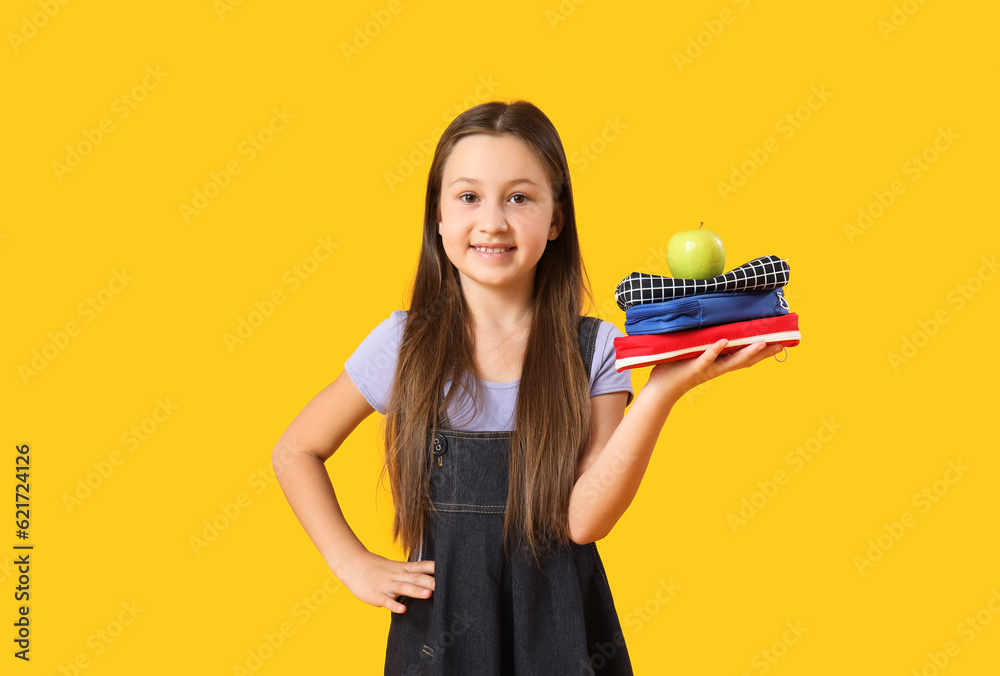 Little girl with pencil cases and apple on yellow background