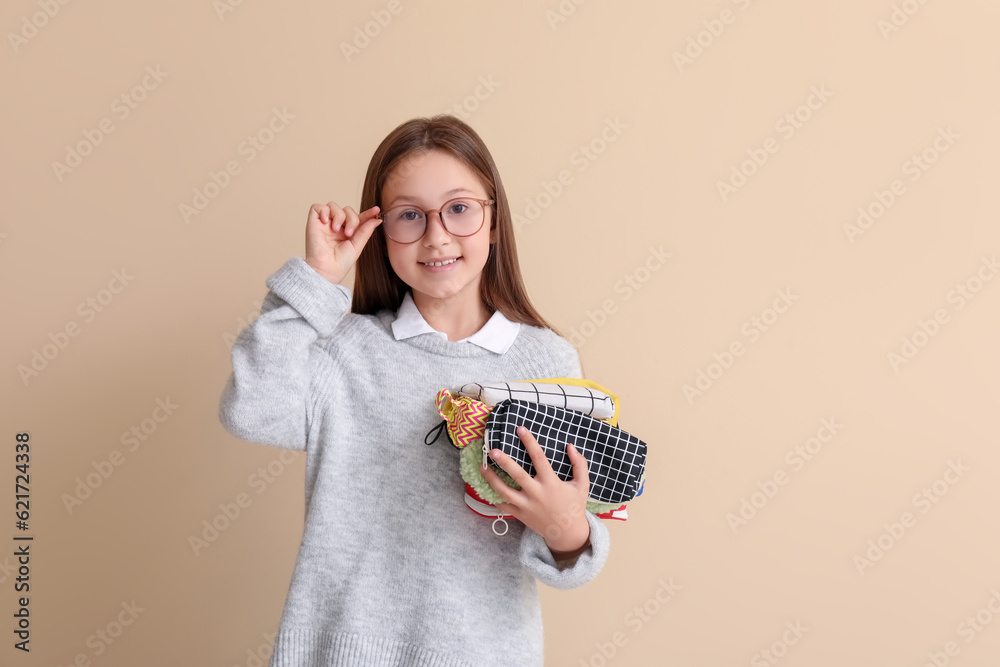 Little girl with pencil cases on beige background