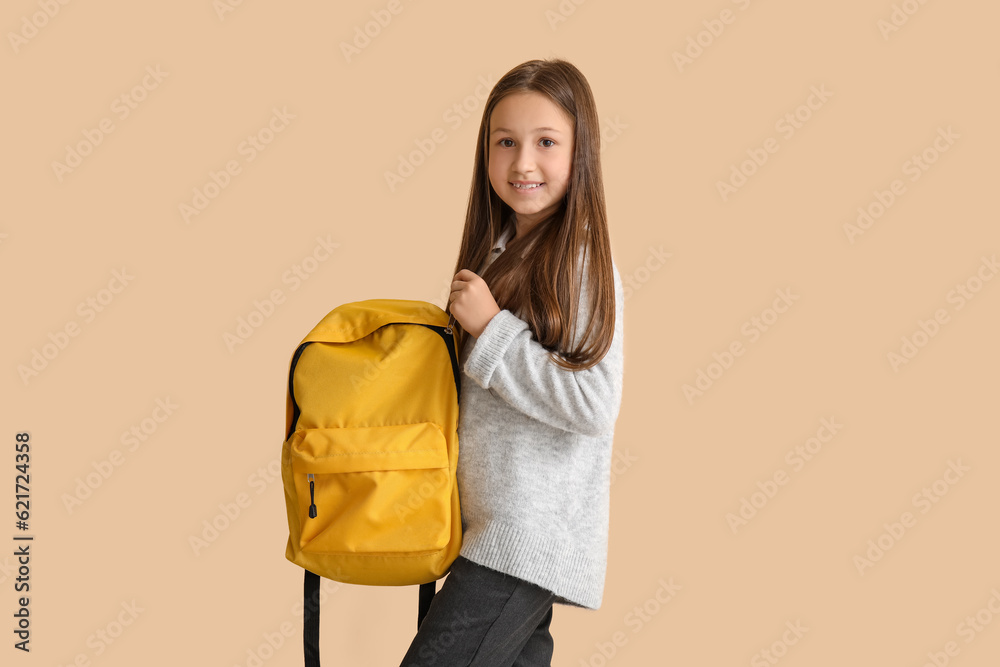 Little schoolgirl with backpack on beige background