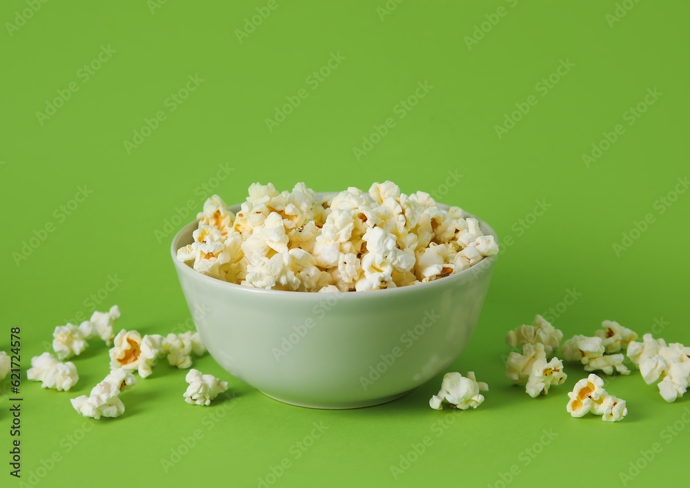 Bowl with tasty popcorn on green background