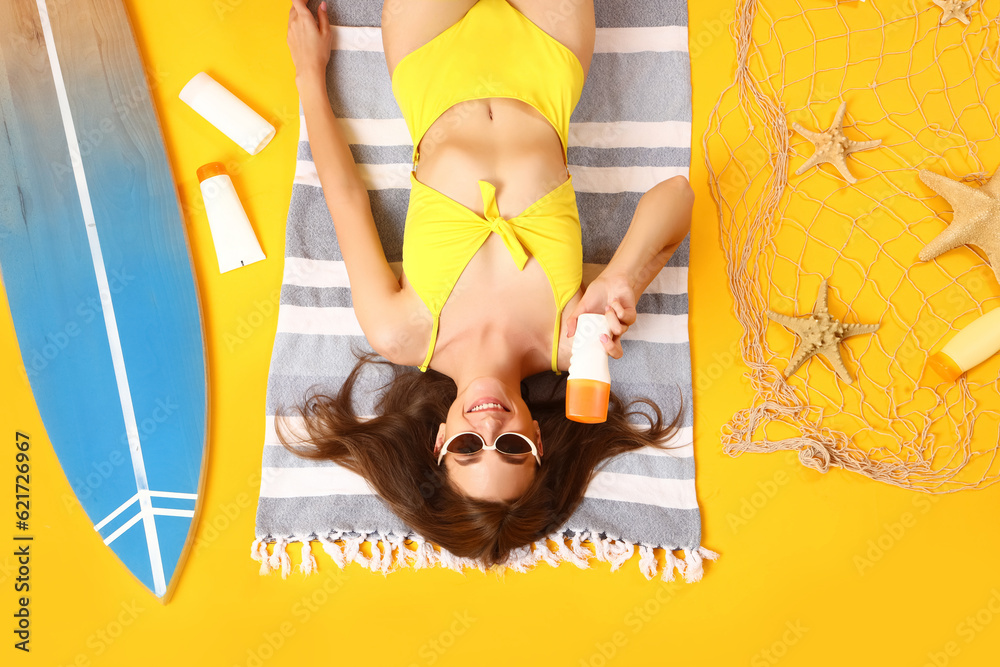 Young woman with sunscreen cream and beach accessories on yellow background, top view