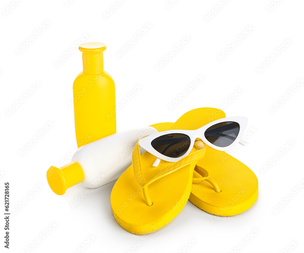 Sunglasses with flip flops and bottles of sunscreen cream isolated on white background