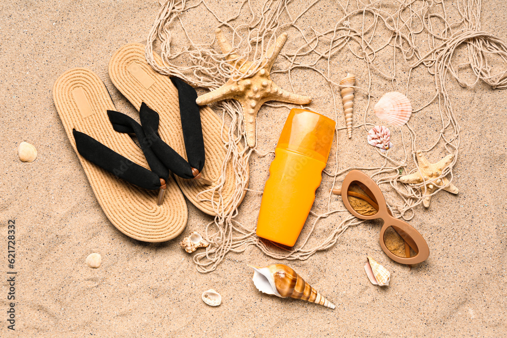 Sunglasses with flip flops, net and bottle of sunscreen cream on sand