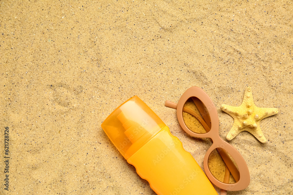 Sunglasses with bottle of sunscreen cream and starfish on sand