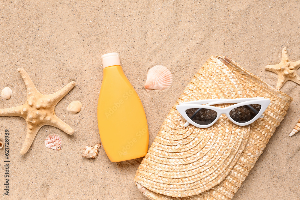 Sunglasses with wicker bag, starfishes and bottle of sunscreen cream on sand