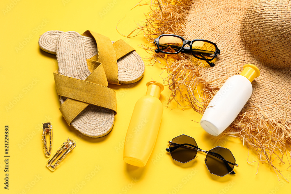 Sunglasses with bottles of sunscreen cream and beach accessories on yellow background