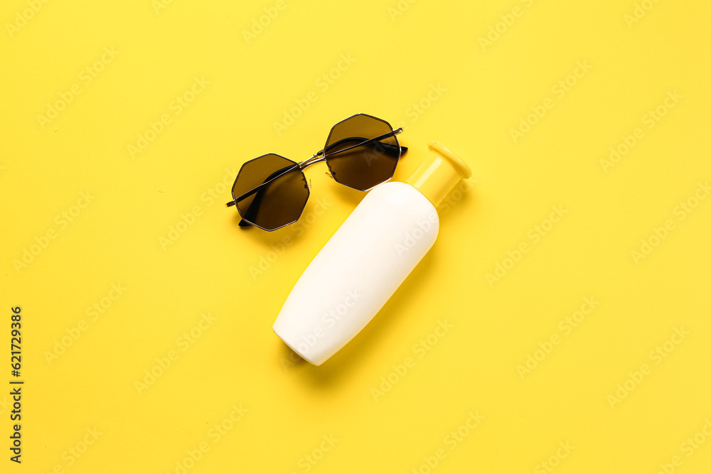 Sunglasses with bottle of sunscreen cream on yellow background