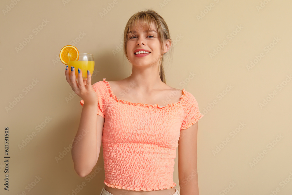 Teenage girl with glass of orange juice on beige background