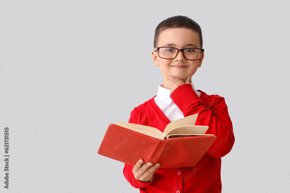 Little schoolboy with book on grey background