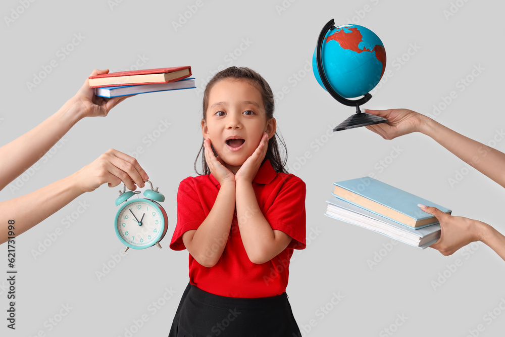 Little schoolgirl and hands holding books, globe and alarm clock on grey background