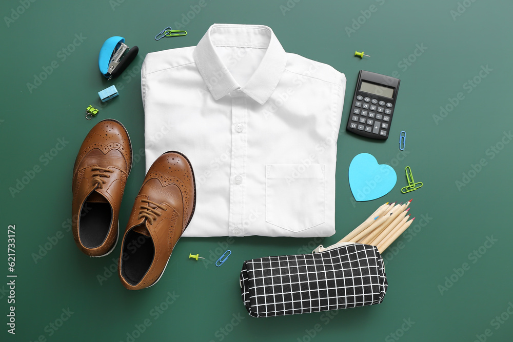 Stylish school uniform with different stationery on green chalkboard