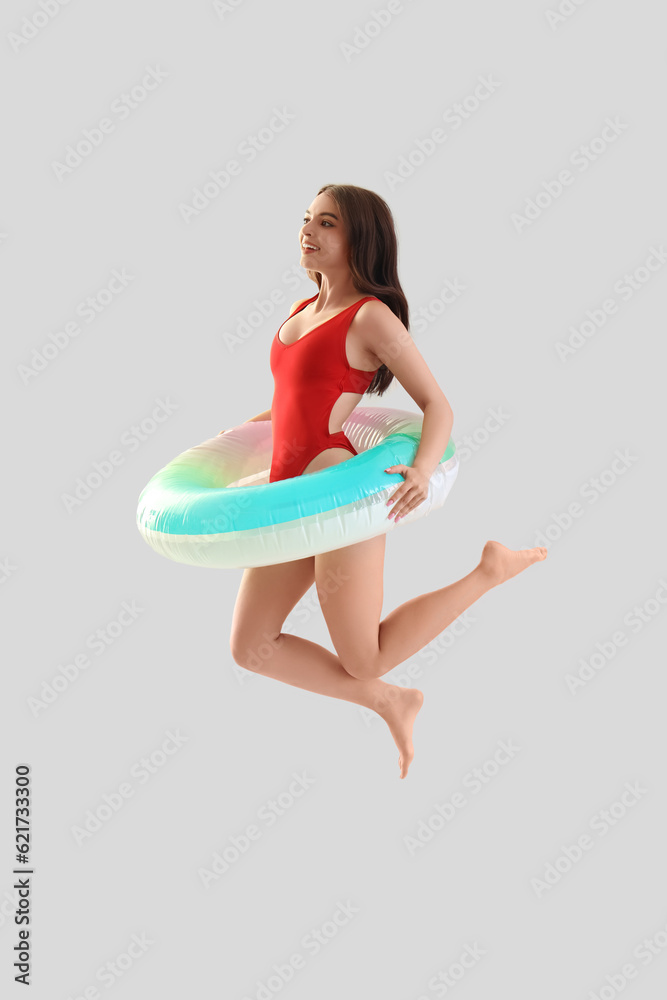 Young woman in swimsuit with inflatable ring jumping on light background