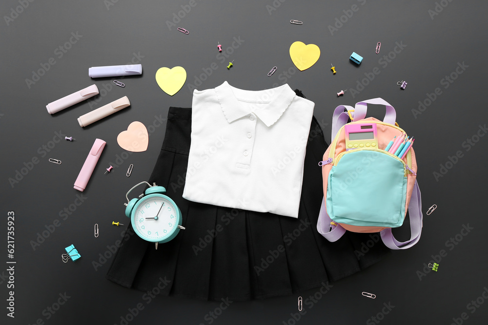 Backpack with different stationery and stylish school uniform on black chalkboard